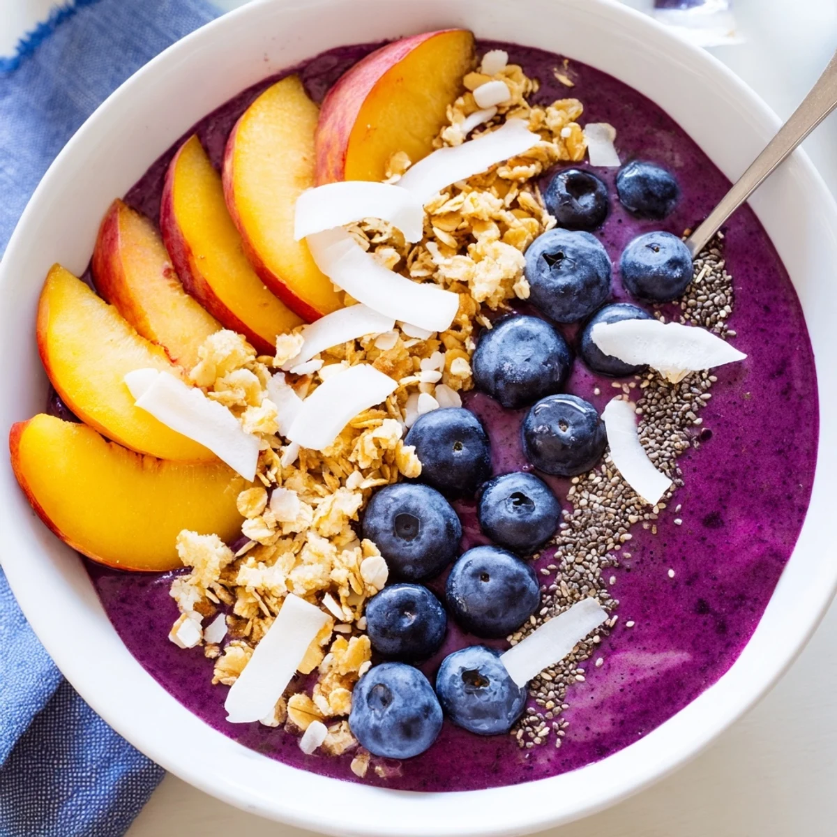 Creamy blueberry peach coconut smoothie bowl topped with crunchy granola and fresh fruit