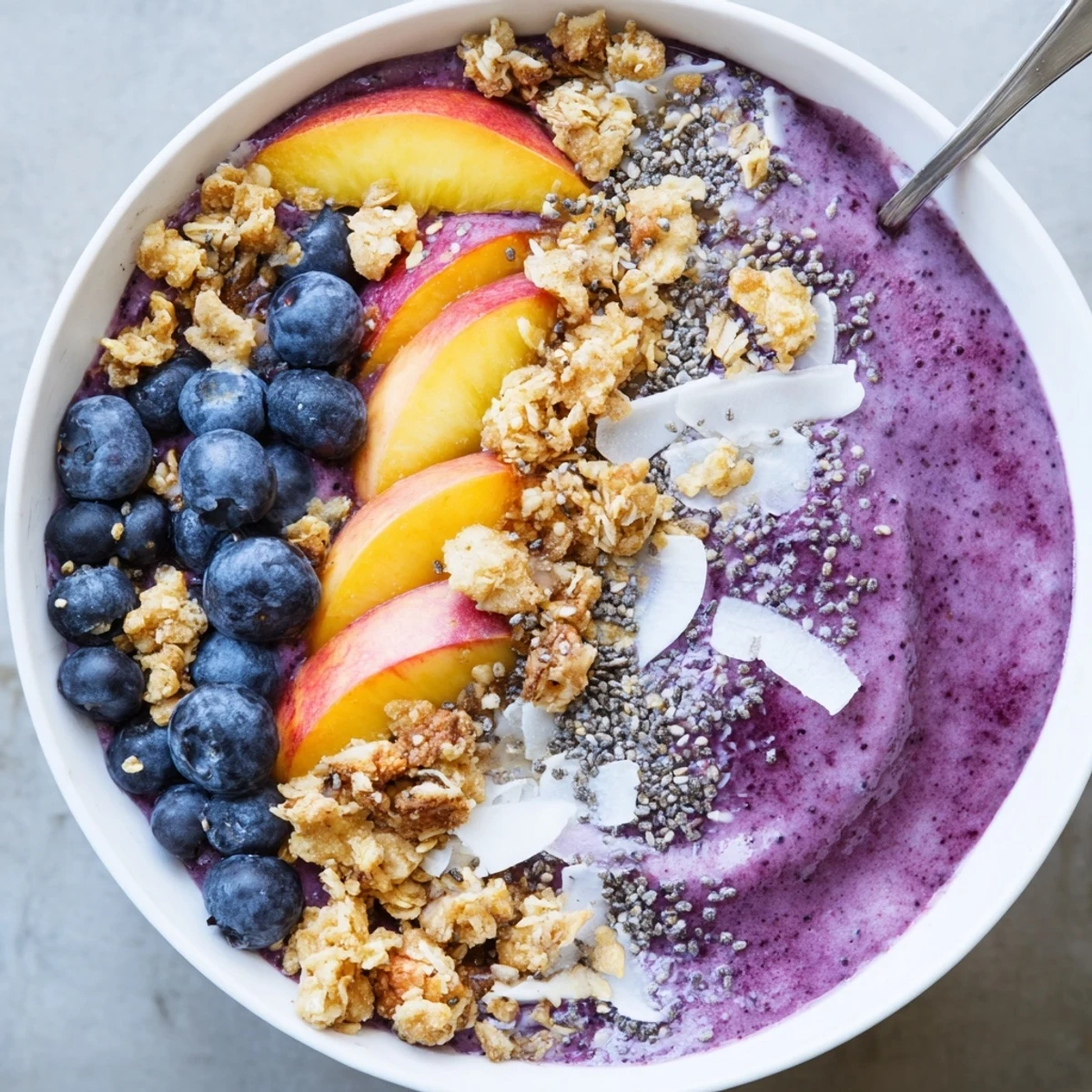 Thick coconut smoothie base with sweet blueberries, peaches, and crispy granola garnish