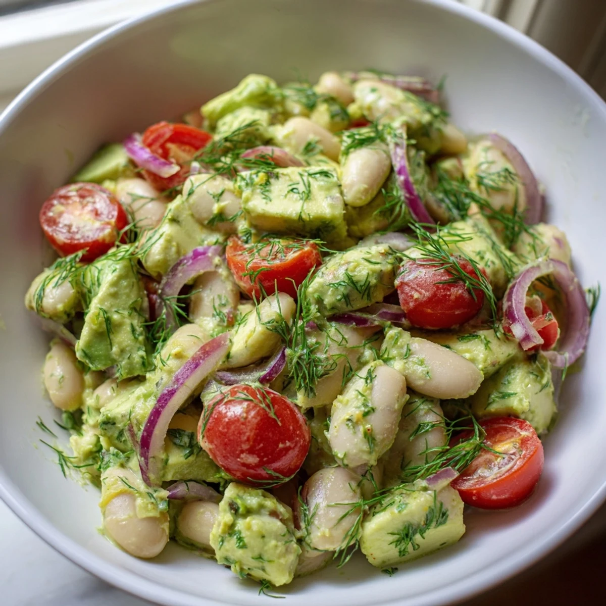 Vibrant white bean salad bowl featuring diced avocado, cherry tomatoes, cucumber, and tangy lemon dill dressing