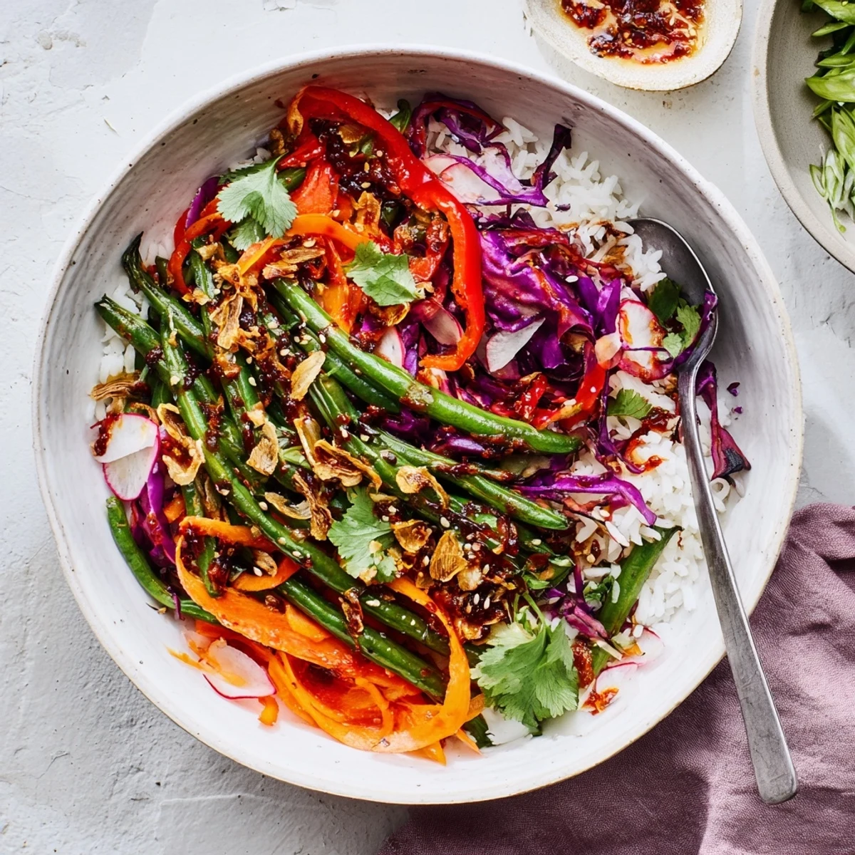 Asian-inspired grain bowl featuring tender roasted green beans drizzled with spicy chili oil and golden fried garlic pieces