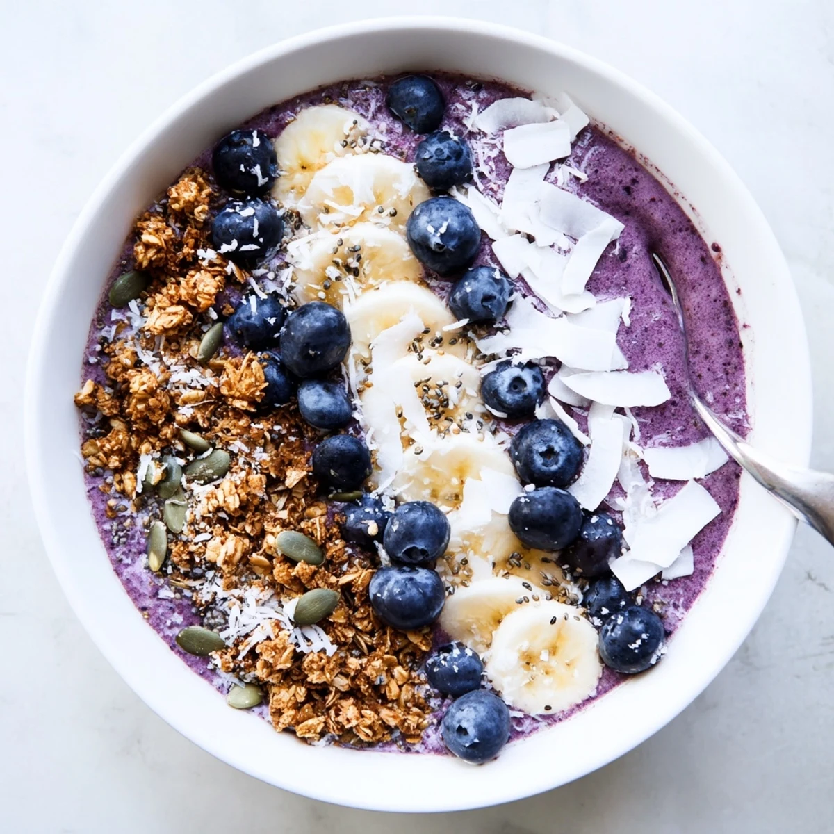 Thick blueberry banana coconut smoothie bowl topped with crunchy granola and fresh fruit