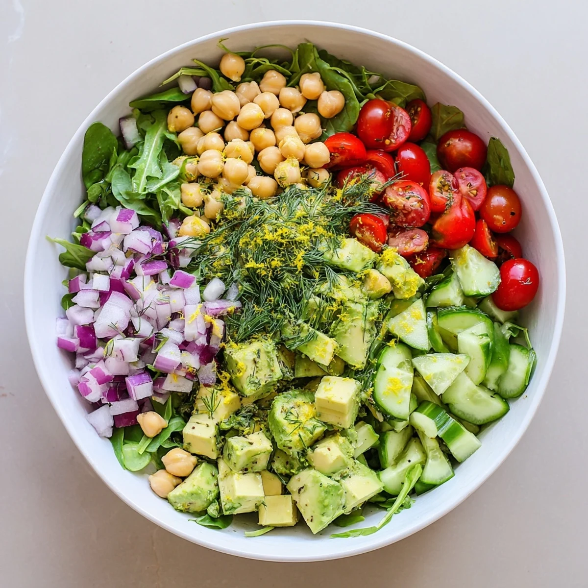 Colorful creamy avocado dill chickpea salad bowl topped with fresh lemon zest and herbs