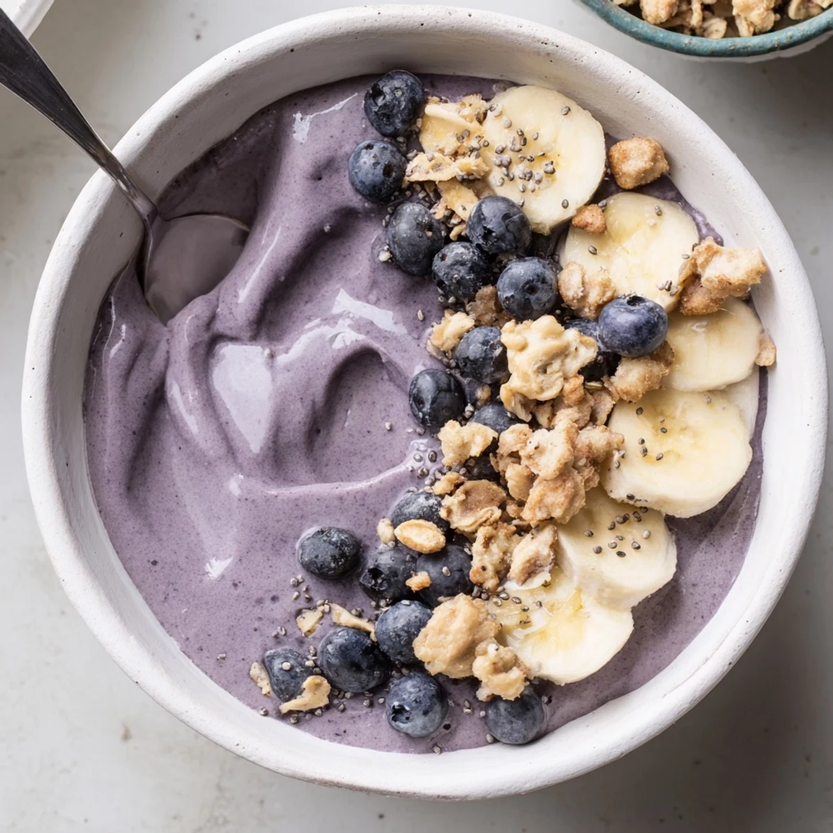 Bright purple Blueberry Banana Cashew Smoothie Bowl with Granola Clusters served chilled