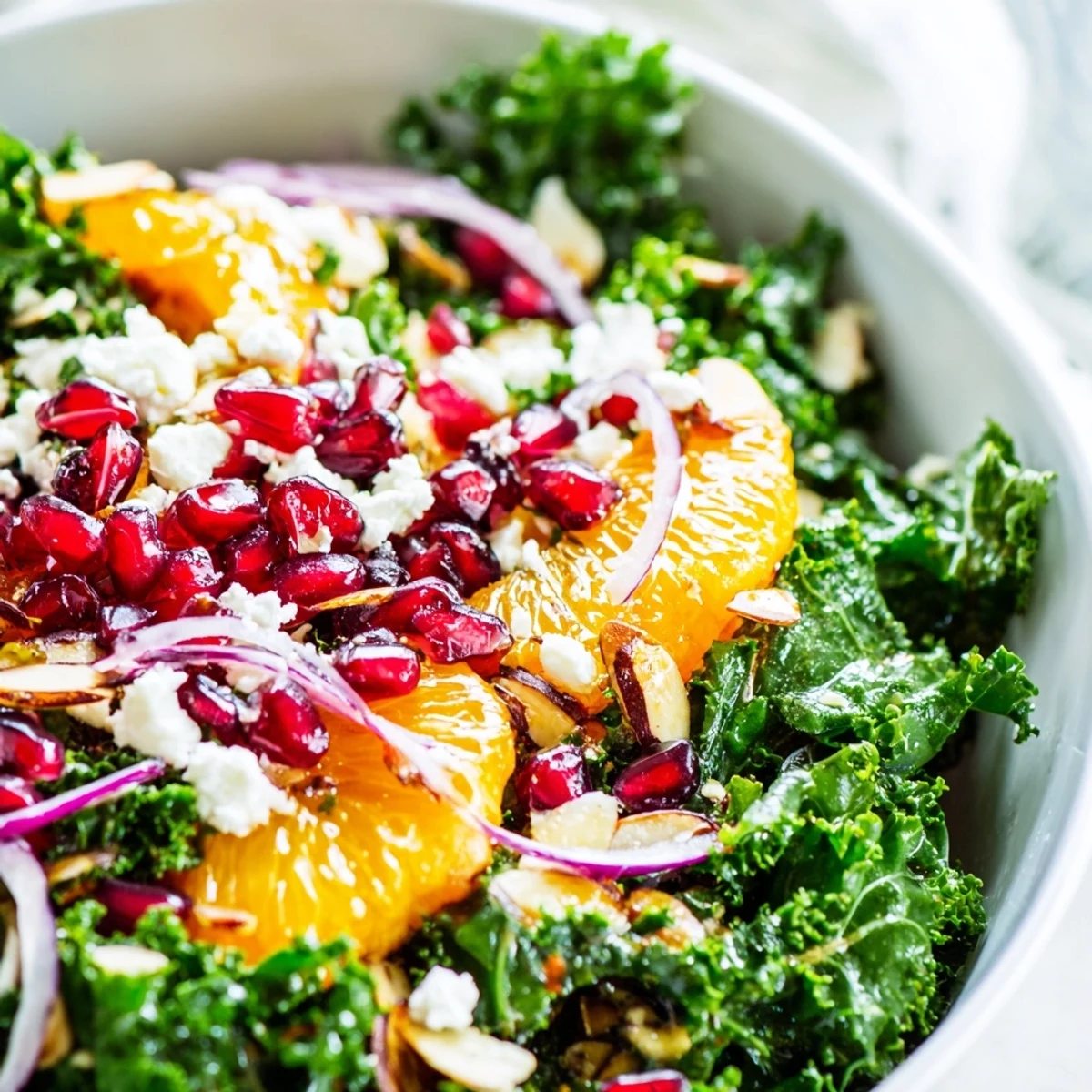 Colorful shaved kale orange almond salad bowl drizzled with zesty citrus dressing and garnished with pomegranate seeds
