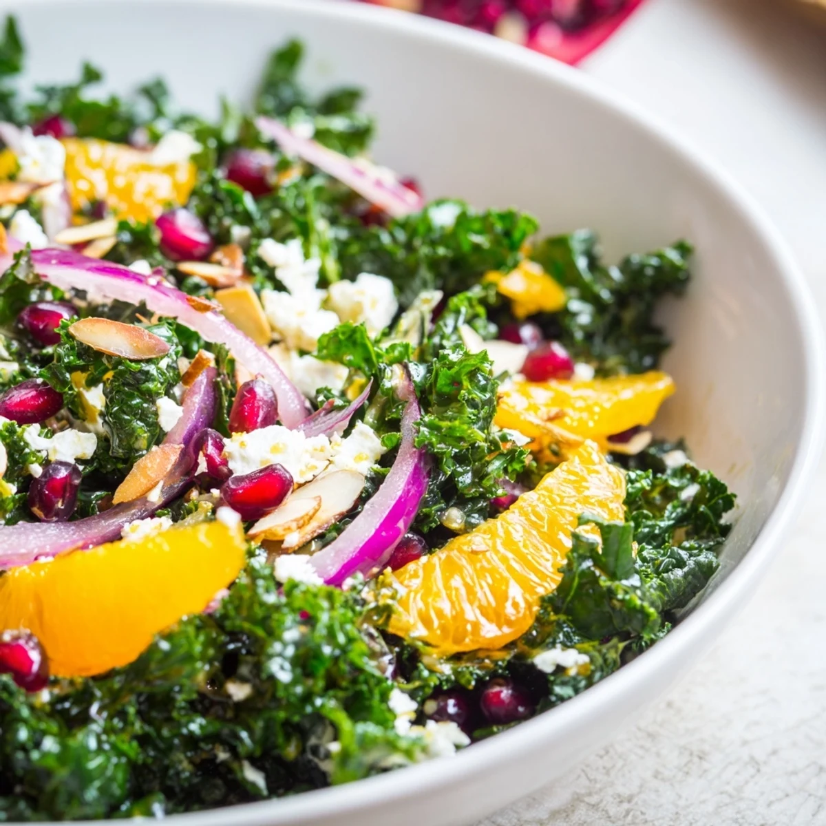 Fresh shaved kale salad bowl featuring juicy orange segments and crunchy toasted almonds in a bright citrus dressing