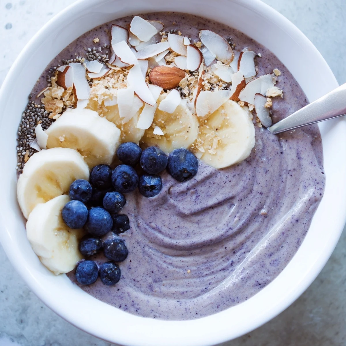 Spoon-ready Blueberry Banana Almond Smoothie Bowl with Coconut Flakes beside coffee