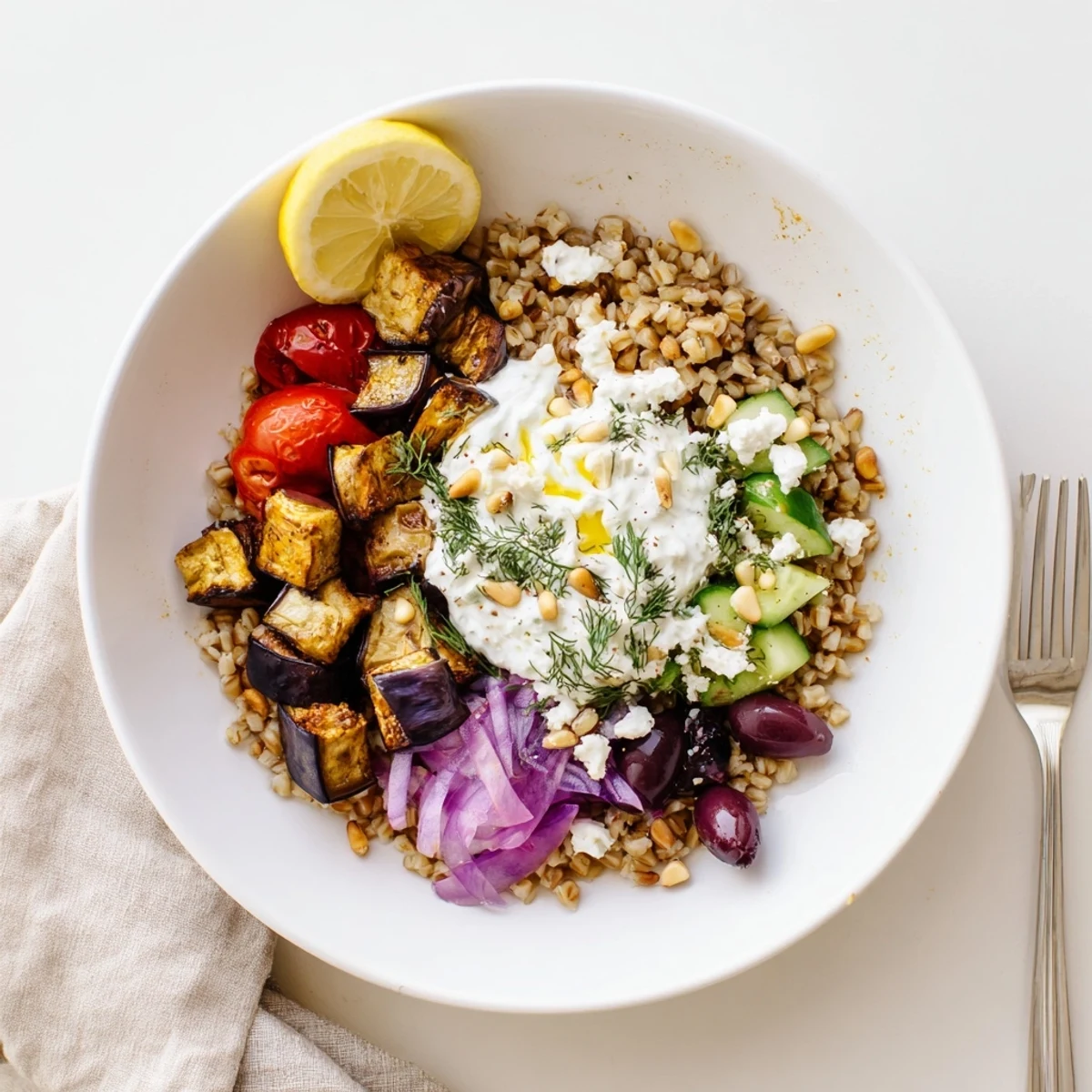 Creamy herb yogurt drizzles over a vibrant Mediterranean roasted eggplant farro grain bowl with fresh vegetables.