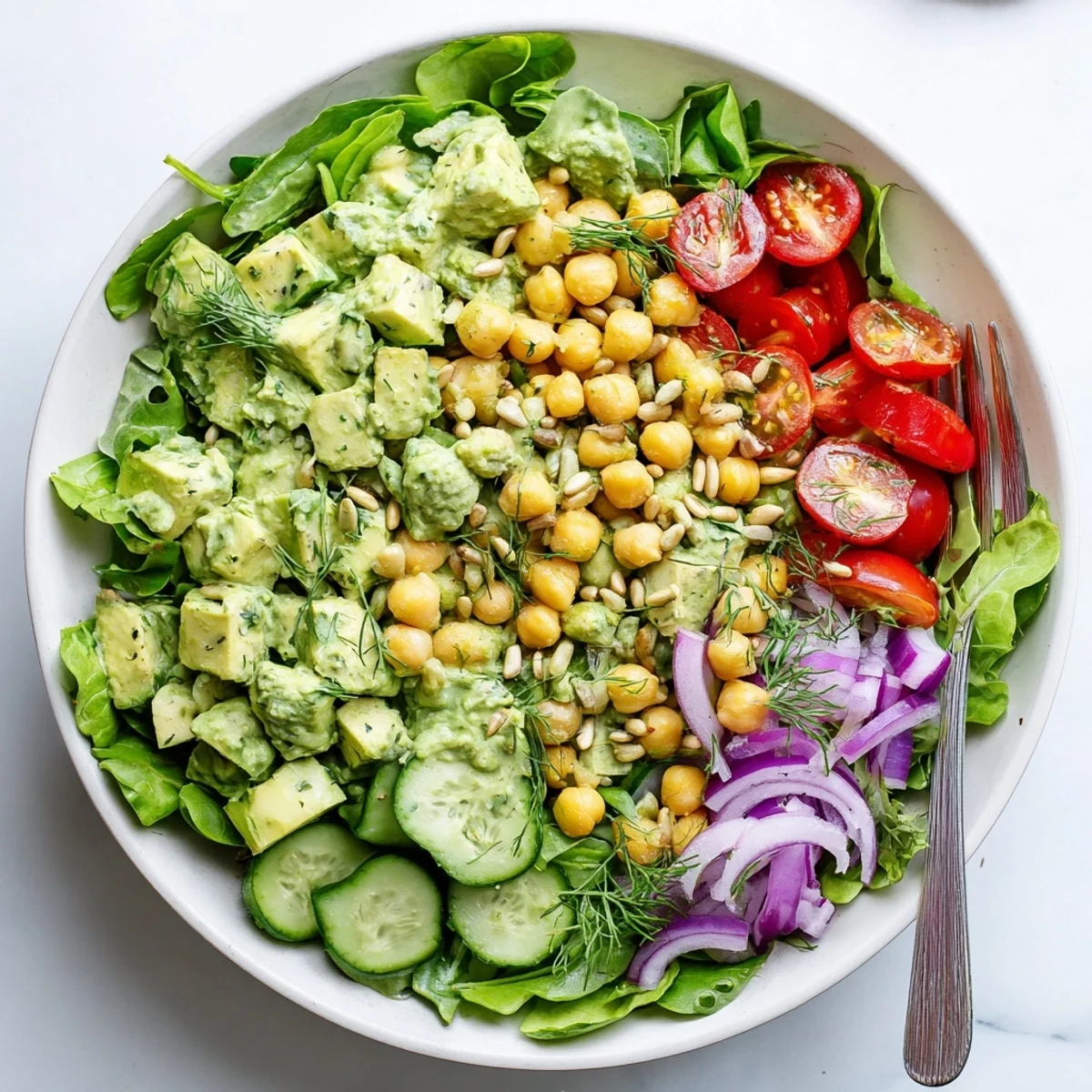 Hearty avocado dill chickpea salad bowl drizzled with tangy yogurt dressing over leafy greens