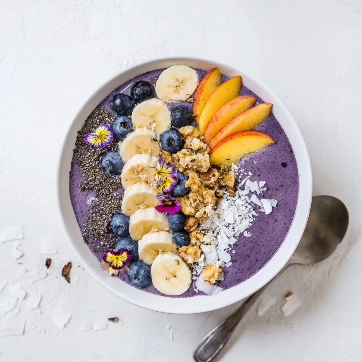 Thick blueberry peach coconut smoothie bowl topped with golden crunchy almond crumble and fresh fruit