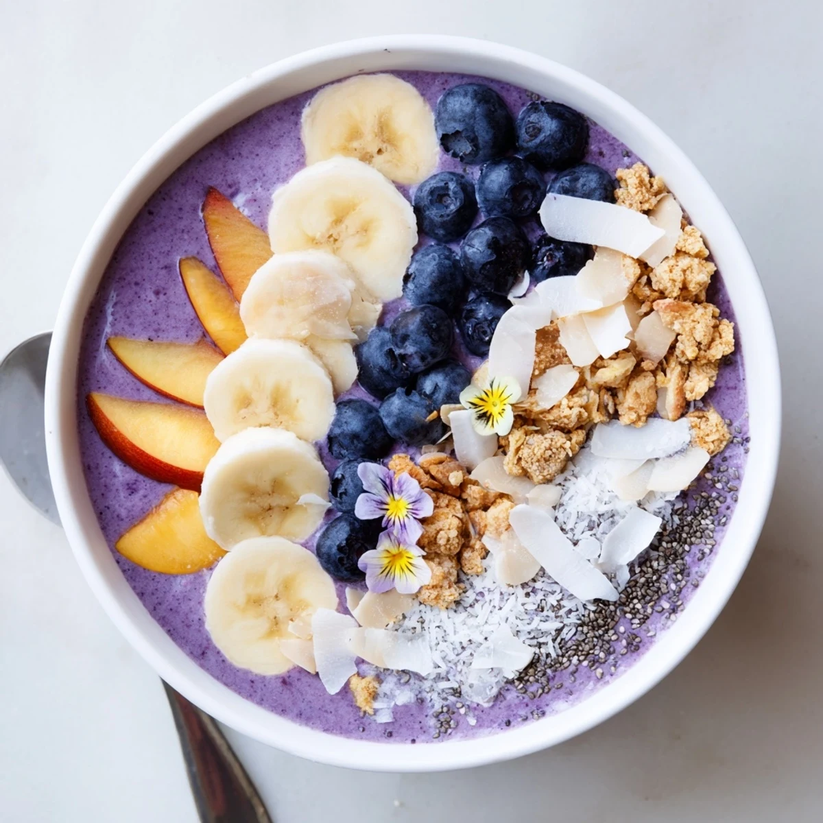 Vibrant purple smoothie bowl loaded with blueberries, ripe peaches, and toasted coconut almond crumble