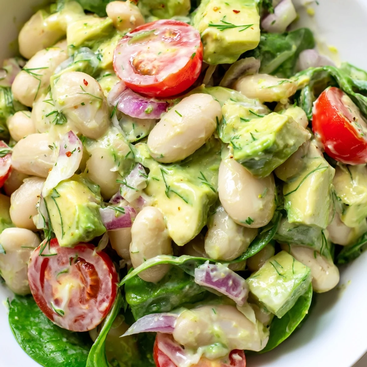 Creamy avocado dill white bean salad served over baby spinach with lemon dressing