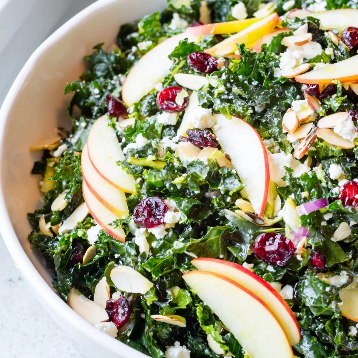 Shaved kale apple almond salad bowl drizzled with bright citrus vinaigrette on rustic pottery