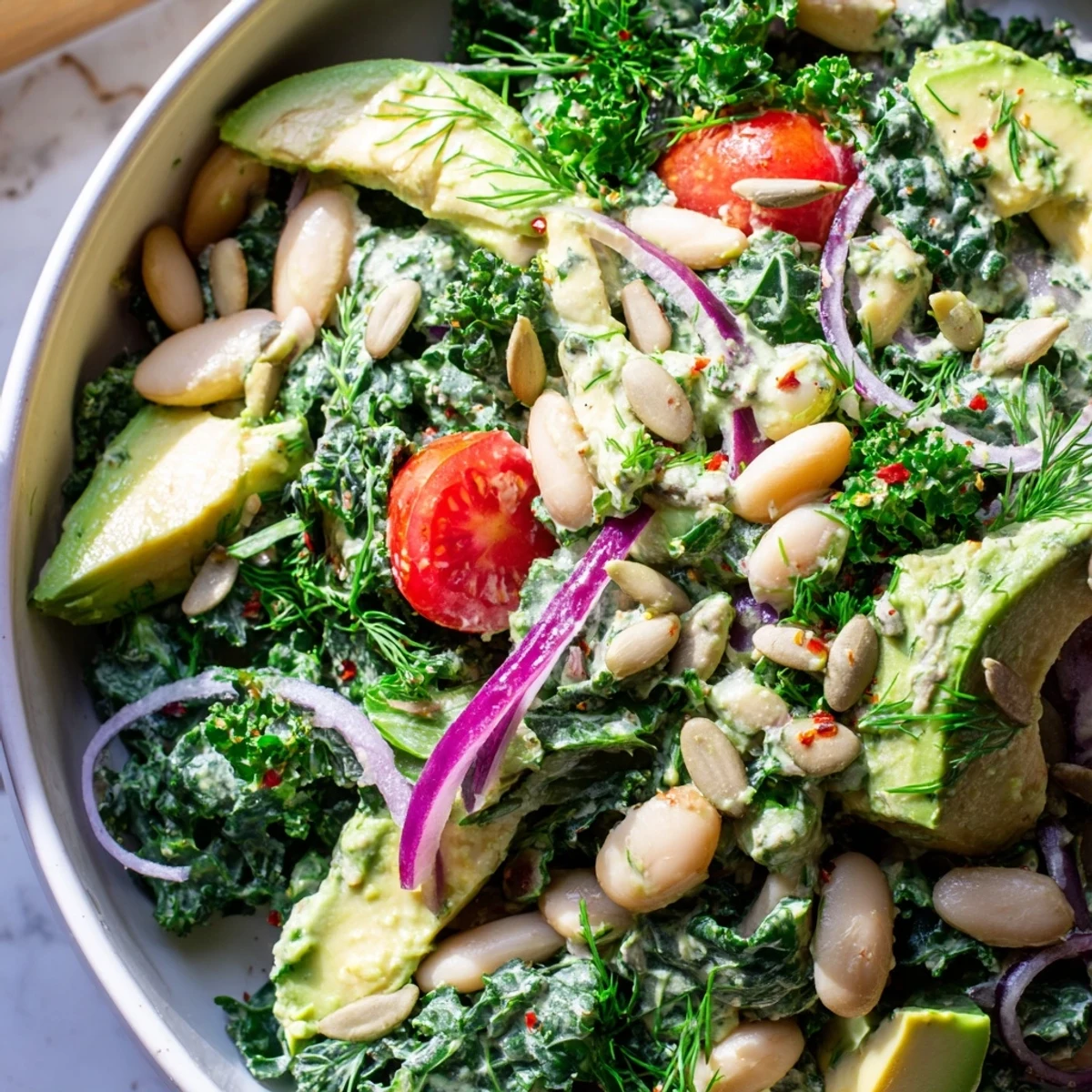 Creamy avocado white bean kale salad bowl topped with toasted pumpkin seeds and herbs