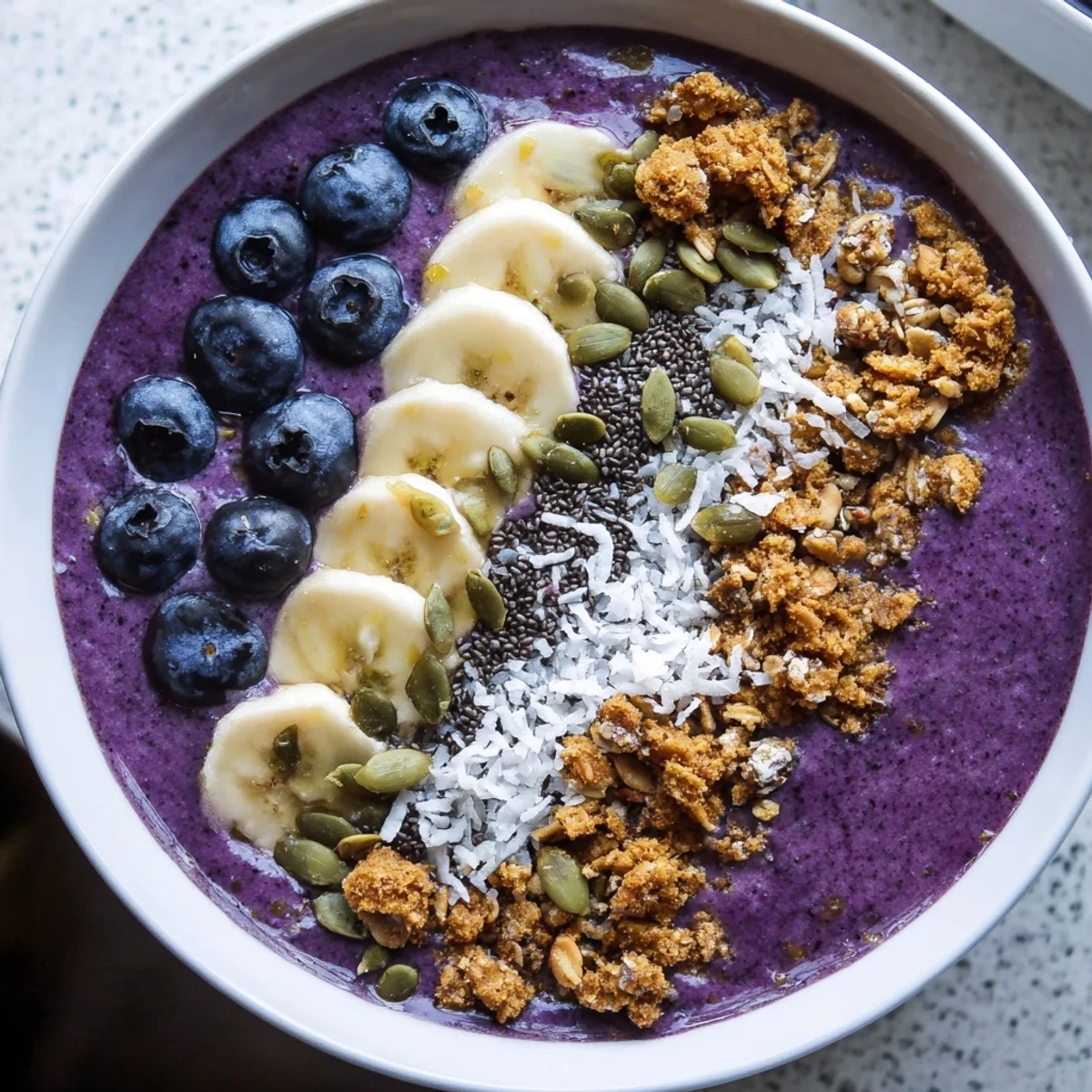 Thick purple smoothie bowl loaded with banana coconut and crunchy granola clusters sprinkled on top