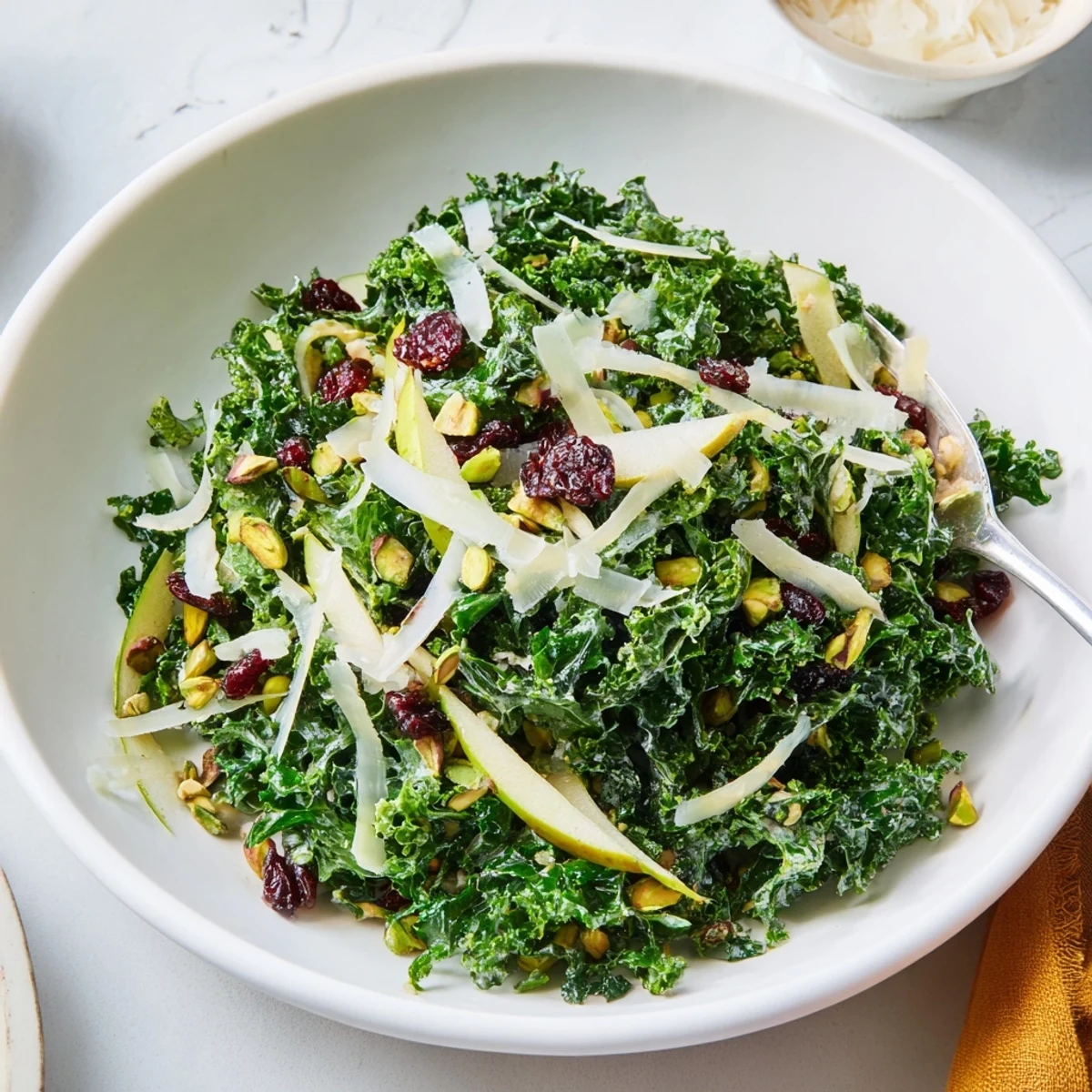 Shaved kale apple pistachio salad in a rustic bowl with cranberries and Parmesan