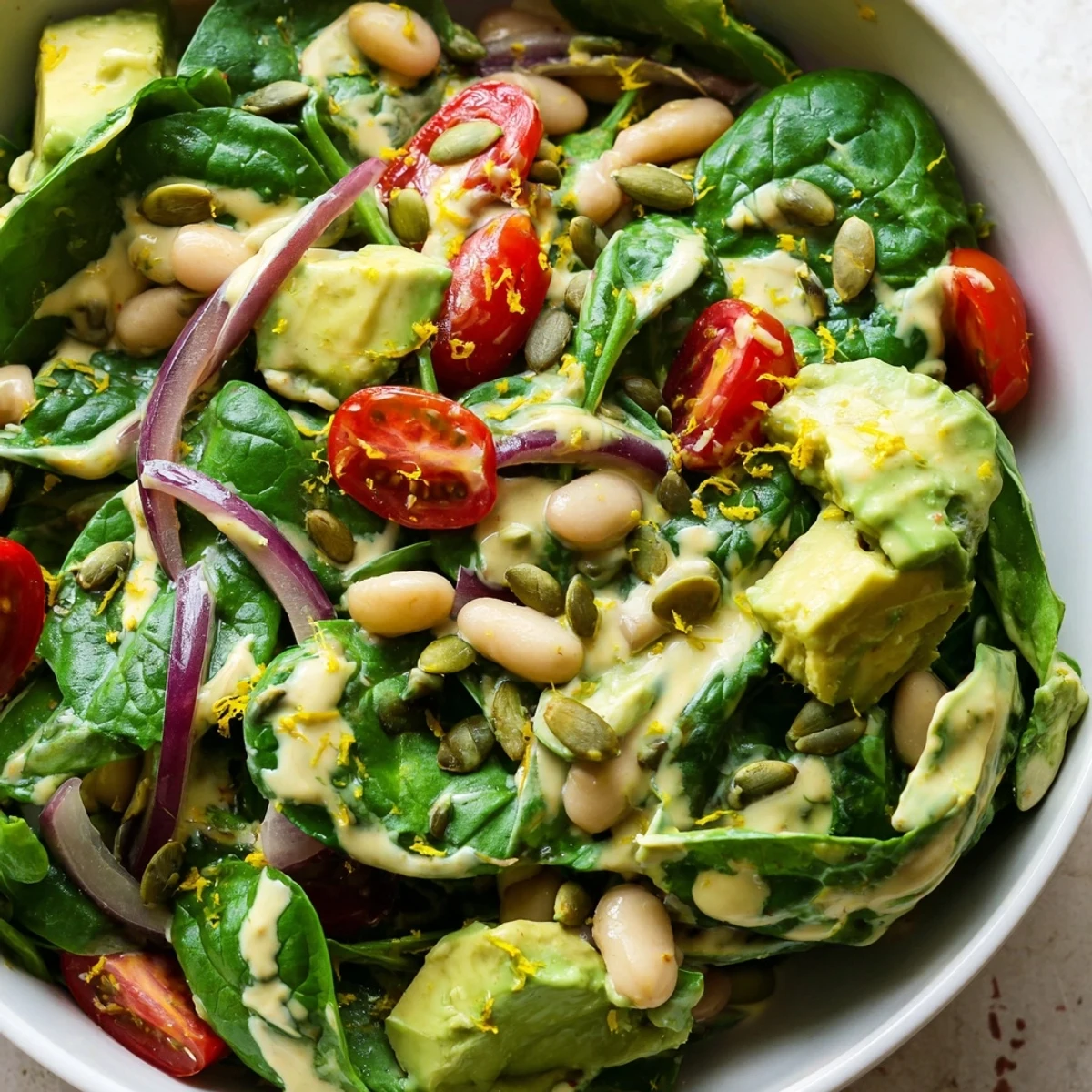 Vibrant spinach salad bowl with diced avocado, white beans, cherry tomatoes, and lemon zest