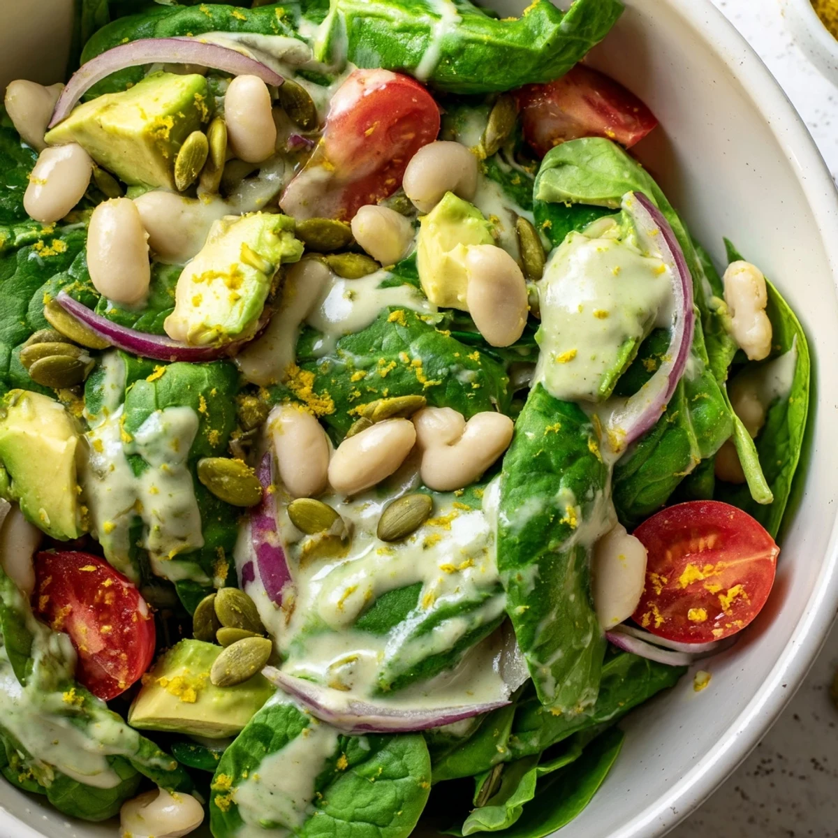 Fresh spinach salad bowl layered with creamy avocado, white beans, and bright lemon zest dressing