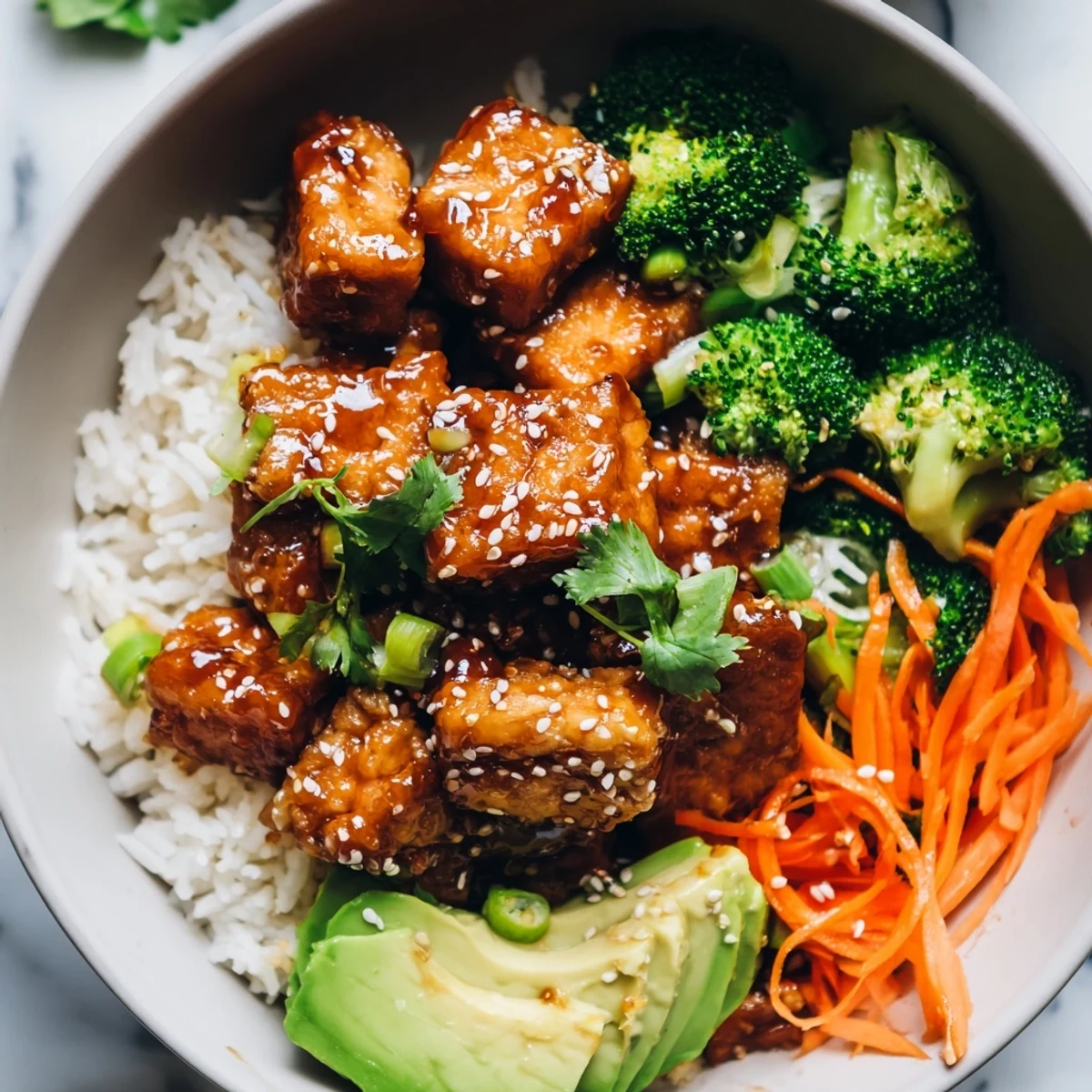 Warm sticky maple soy tempeh Vegan Bowl topped with avocado, carrots, and sesame seeds