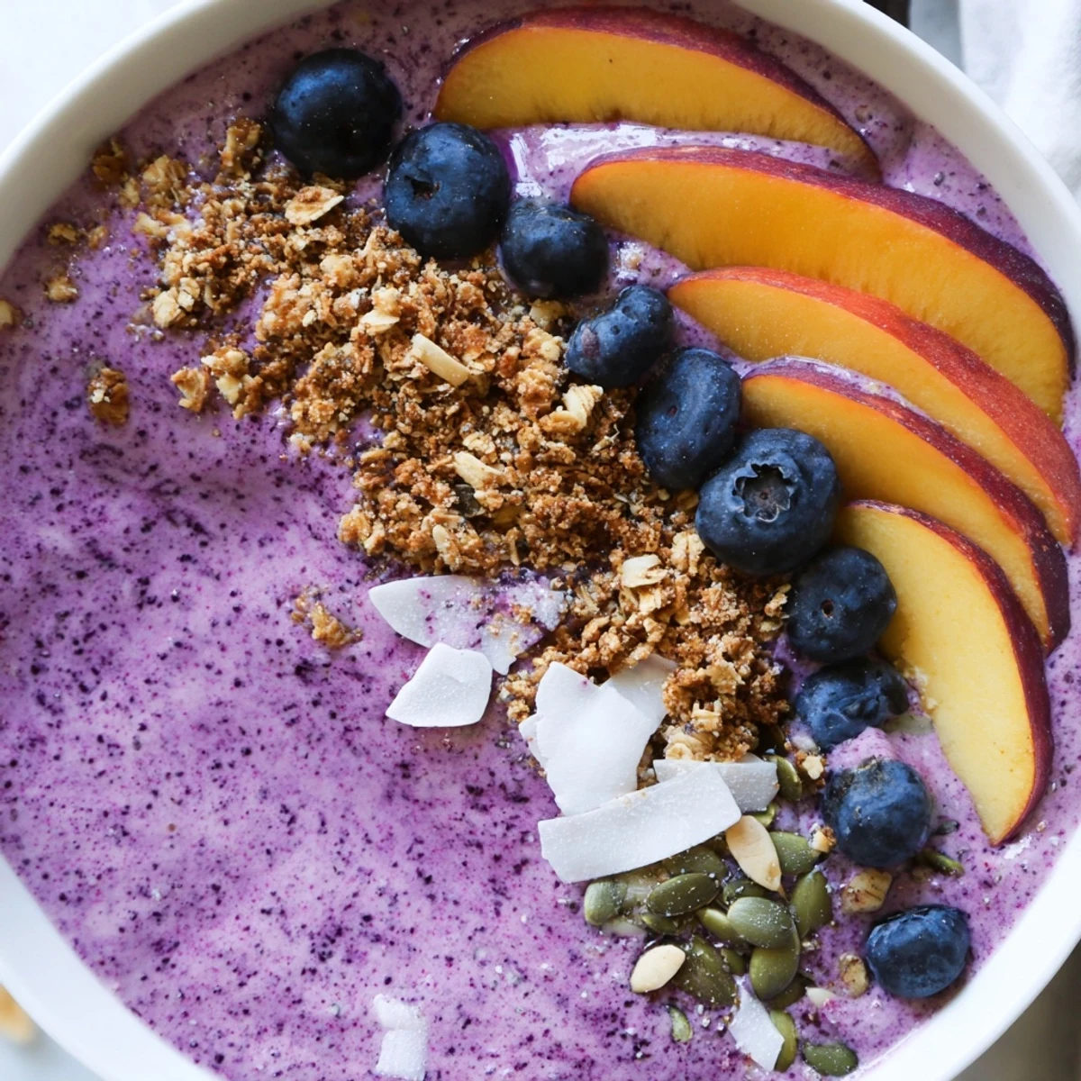Vibrant blueberry peach coconut smoothie bowl in two bowls sprinkled with chia seeds and coconut flakes.