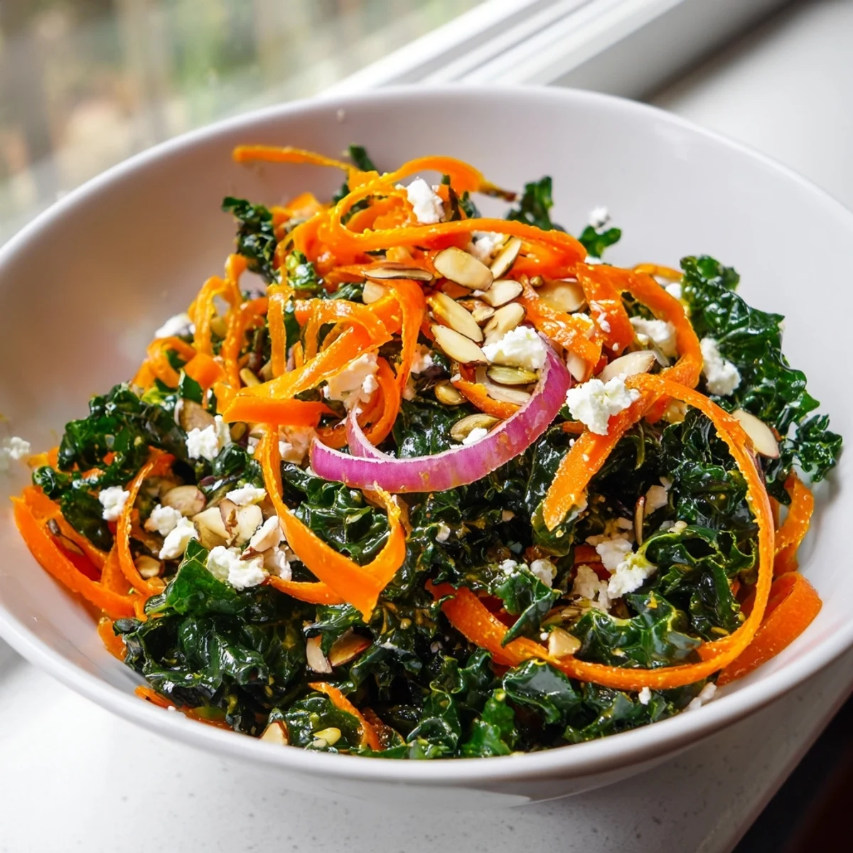 Shaved Kale Carrot Almond Salad Bowl with Citrus Dressing topped with toasted golden almonds and crumbled feta