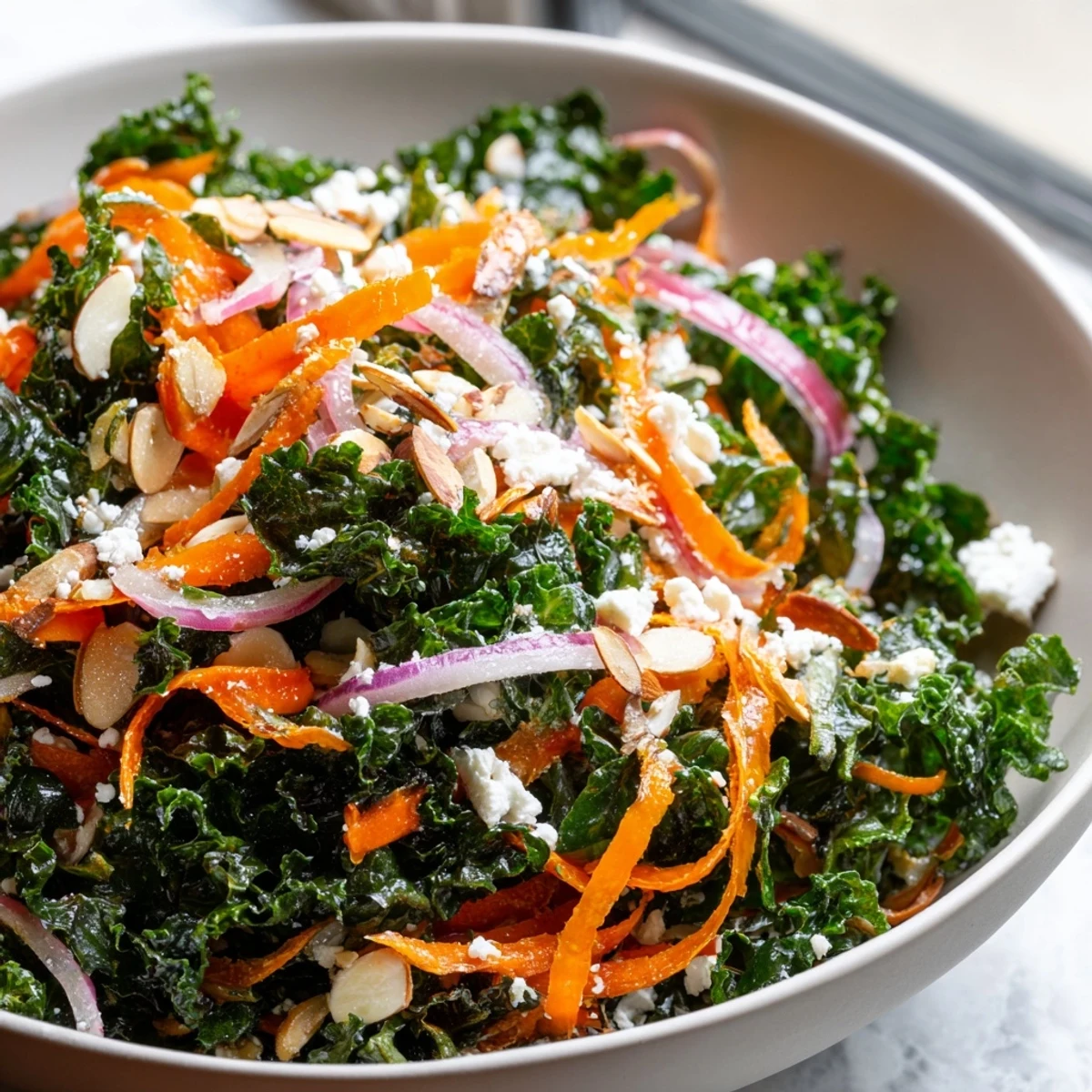 Bright green kale ribbons and julienned carrots tossed in Shaved Kale Carrot Almond Salad Bowl with Citrus Dressing