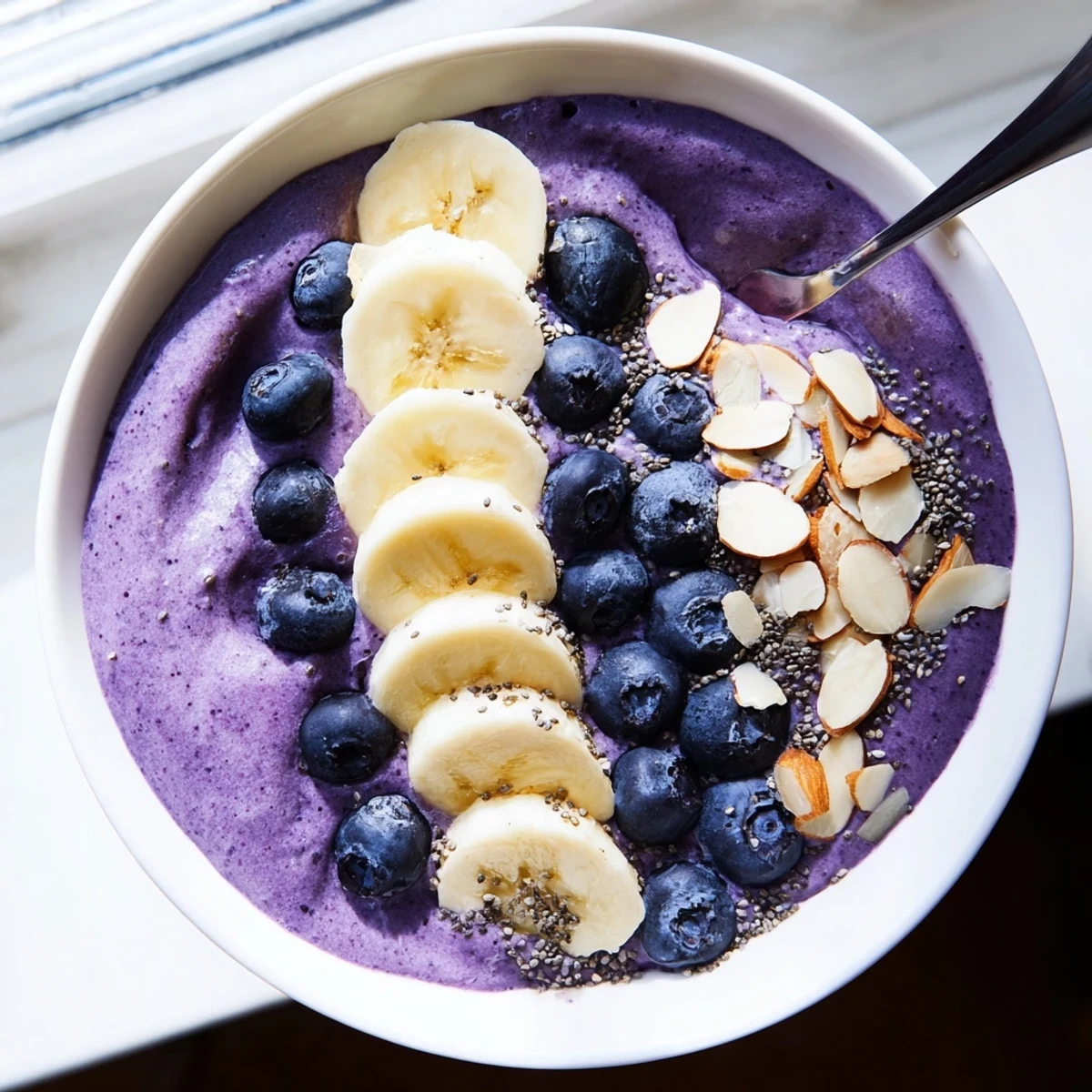 Creamy blueberry banana almond smoothie bowl topped with toasted coconut flakes and fresh berries