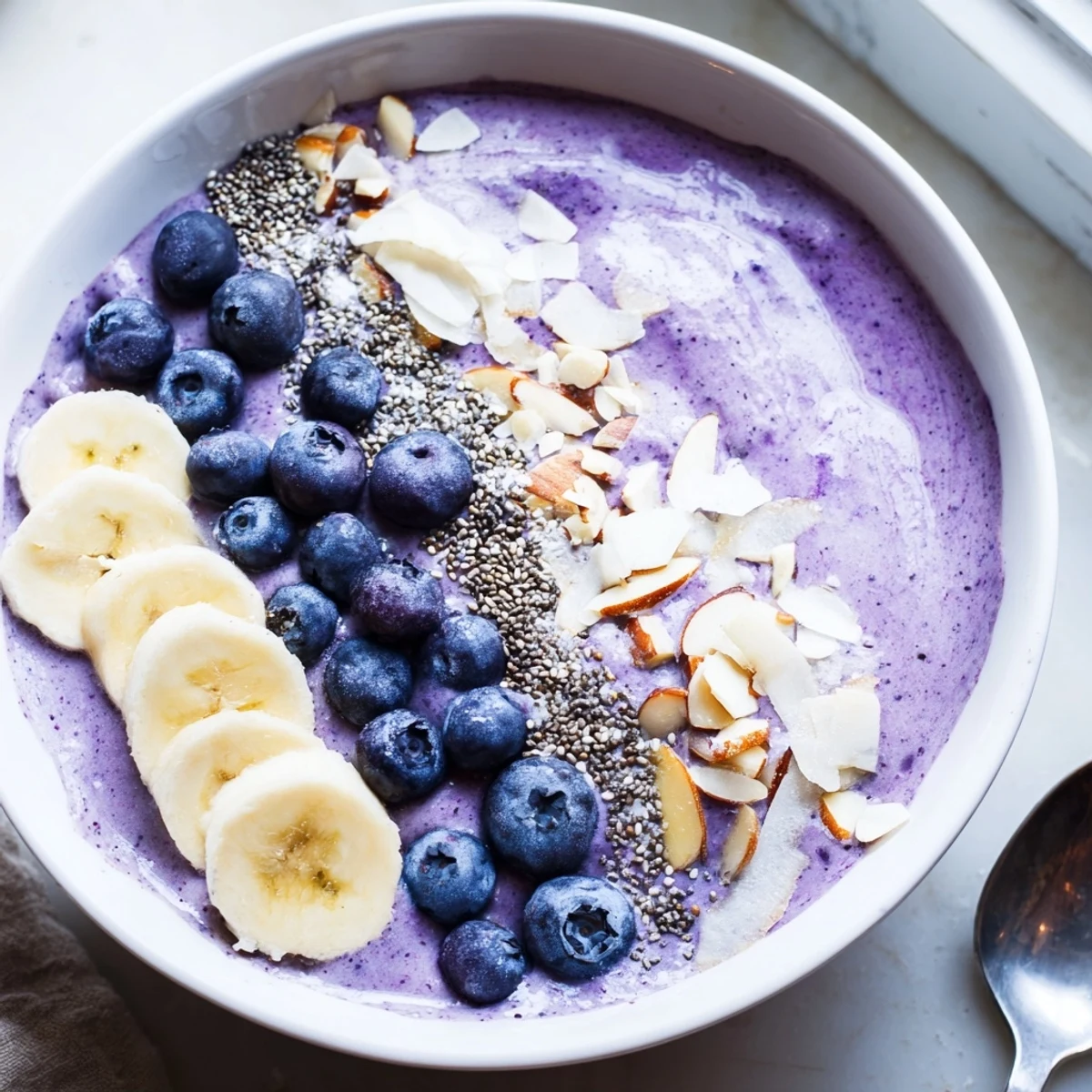 Vibrant purple blueberry banana almond smoothie bowl drizzled with almond butter and coconut