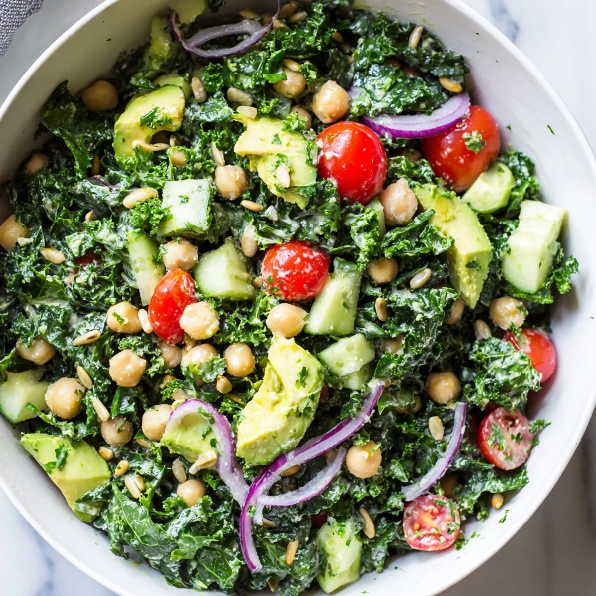 Creamy avocado chickpea kale salad bowl topped with golden roasted seeds and bright lemon zest dressing