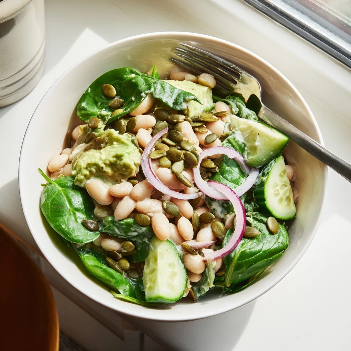 A bowl of creamy avocado dill white bean salad topped with crisp cucumber slices and toasted pumpkin seeds for a refreshing lunch.