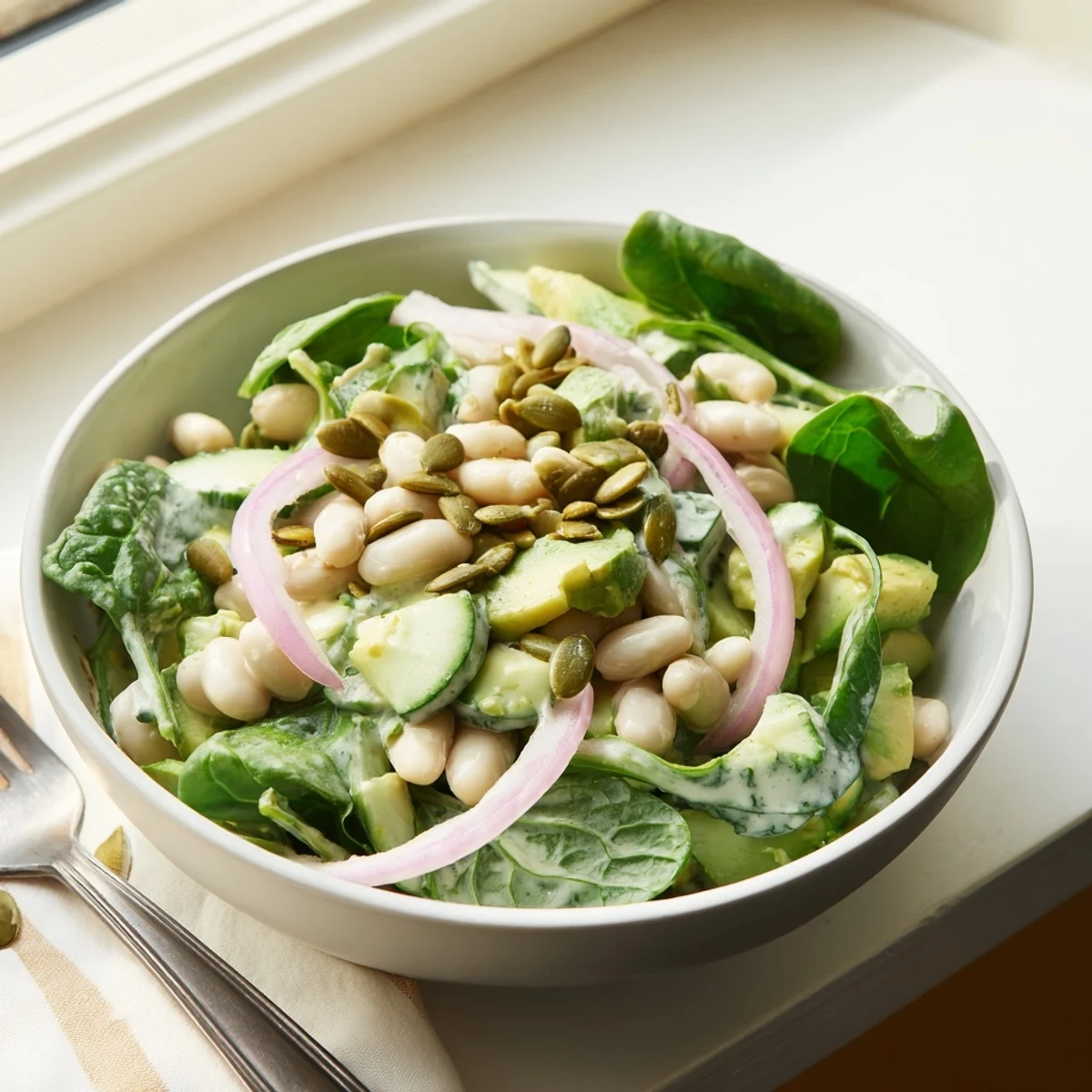 Close up of protein packed avocado dill white bean salad with fresh dill and crunchy cucumbers served in a rustic bowl.