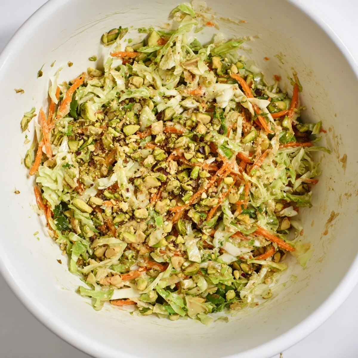 Vibrant lunch bowl with shaved cabbage carrots toasted pistachios drizzled with sesame tahini dressing