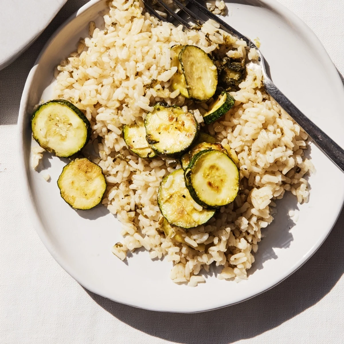 Close-up of fluffy Garlic Lemon Herb Brown Rice topped with tender roasted zucchini rounds and red pepper flakes on a wooden board