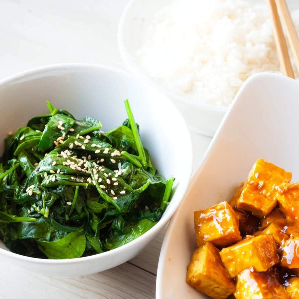 A close-up of sticky orange soy tofu bowl with wilted sesame greens and spring onions.