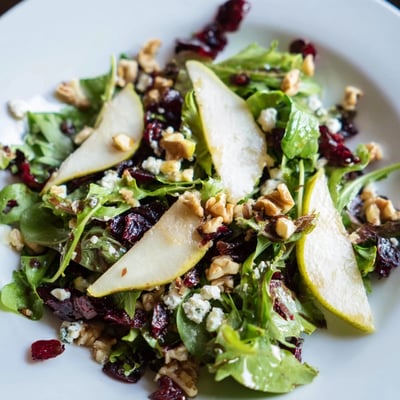 Cranberry Pear Greens salad featuring vibrant greens, sweet pear slices, crunchy toasted pecans, tart cranberries, and a tangy apple cider vinaigrette.