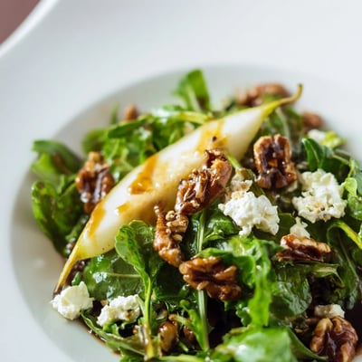 Candied pecans and creamy goat cheese garnish a fresh bowl of Harvest Pear Greens salad with balsamic vinaigrette.
