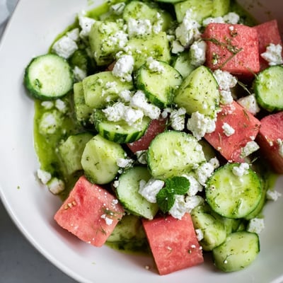 Colorful summer salad bowl featuring chilled watermelon cubes, sliced cucumbers, and creamy feta cheese dressed with herbaceous mint oil for a refreshing bite.