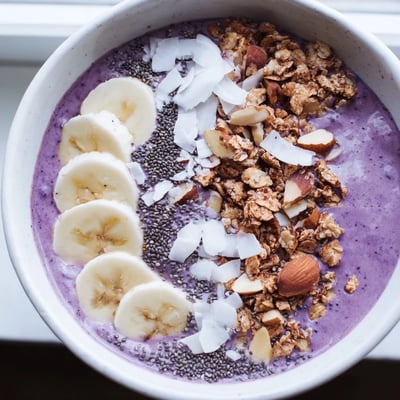 A close view of creamy ube banana coconut smoothie bowl with granola, chia seeds, and toasted nuts.  