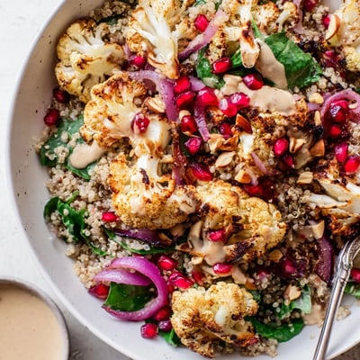 Colorful Roasted Cauliflower Pomegranate Quinoa Grain Bowl with Tahini Drizzle served warm on greens