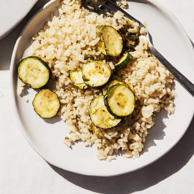 Close-up of fluffy Garlic Lemon Herb Brown Rice topped with tender roasted zucchini rounds and red pepper flakes on a wooden board